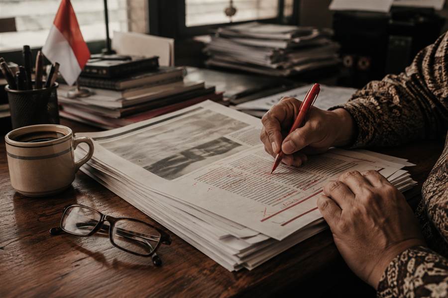 Editor menandai naskah cetak dengan pena tinta merah