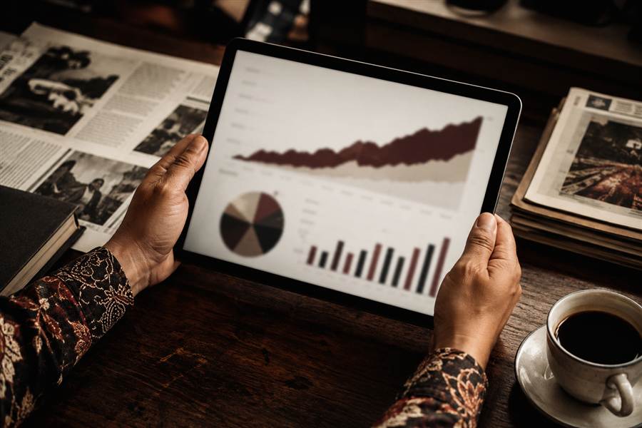 Tangan memegang tablet berisi grafik laporan performa publikasi
